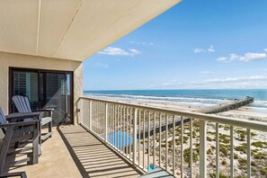 A balcony with chairs and a view of the beach and pier.
