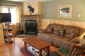 A cozy living room with a stone fireplace, a leather sofa, a wooden coffee table, and a television.