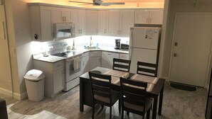 A compact kitchen with white cabinets, a microwave, stove, sink, and a dining area with a table and chairs.