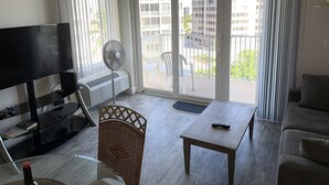 A living room with a flat-screen TV, a standing fan, a wicker chair, a wooden table, and a sofa.