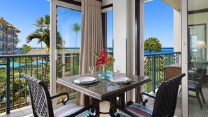 A balcony with a table set for two, overlooking a resort area with palm trees and a clear blue sky. - Waipouli Beach Resort Exquisite Ocean View Condo with Beach Front View (Kapaa)