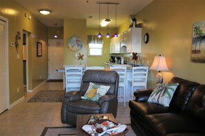 A living room with a leather sofa, a dining area with a table and chairs, and a kitchen with white cabinets and a refrigerator. - Last minute discounts - Steps to the Bay - Baywatch A1 (Pensacola Beach)