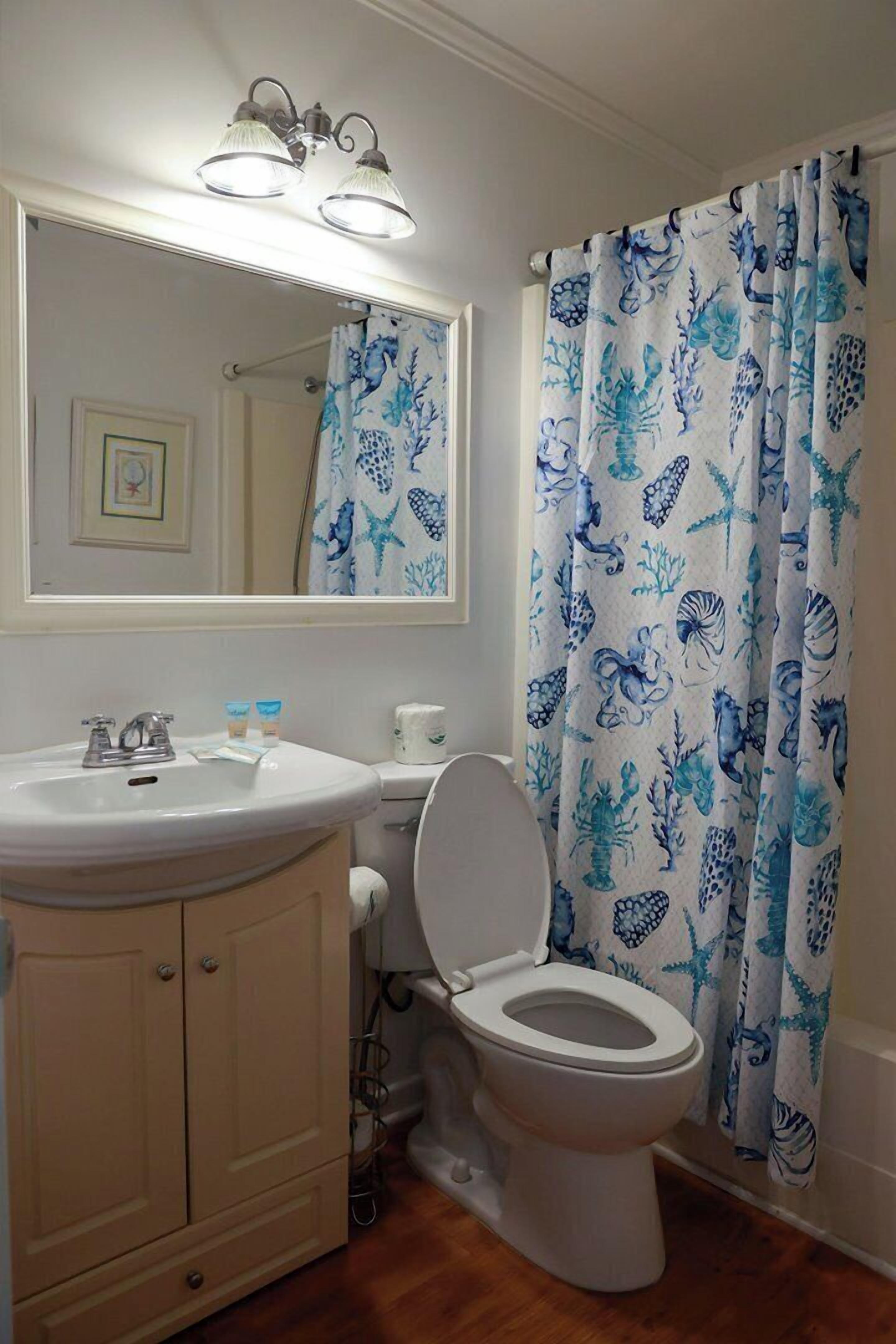 Un baño con un lavamanos blanco, un inodoro y una cortina de ducha con un diseño acuático azul.