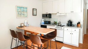 A compact kitchen with white cabinets, a microwave, a stove, and a coffee maker. There are four brown chairs around a wooden table. - On the beach 183 SeaSide Villas (Hilton Head Island)