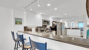 Een moderne keuken met witte kasten, roestvrijstalen apparatuur en een bar met blauwe stoelen.