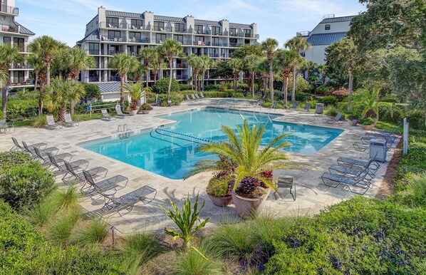 Ein Hotel mit einem großen Pool, umgeben von Liegestühlen und Palmen.