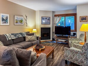 A living room with a sofa, armchairs, a coffee table, a fireplace, a TV, and framed pictures on the wall. - Townhome F4 - Vacation Rental on 4th Lake (Inlet)