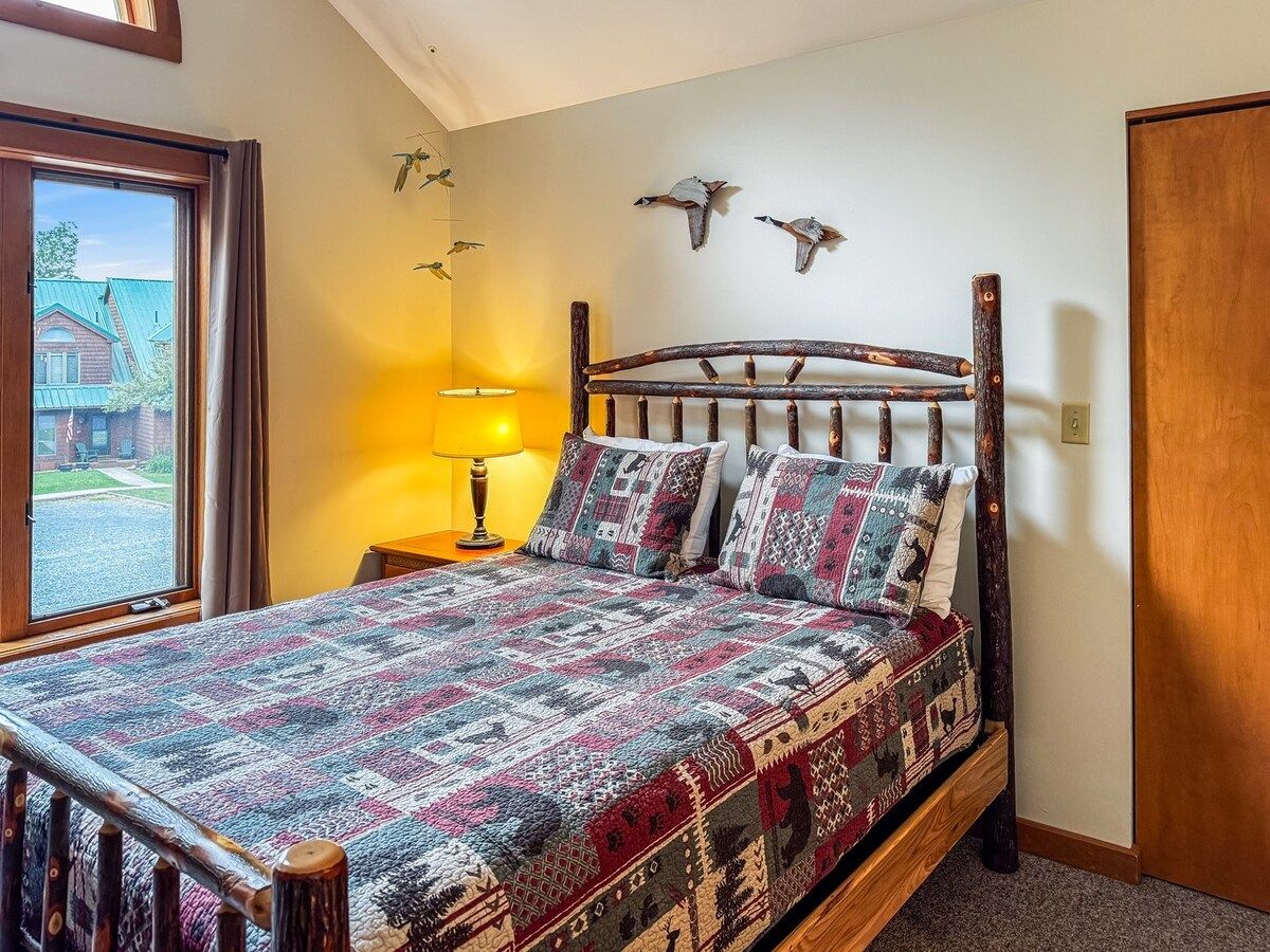 A bedroom with a wooden bed, patterned bedding, a bedside lamp, and wall art.