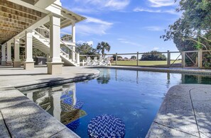 Une piscine dotée d’une terrasse carrelée, d’un espace salon couvert et offrant une vue sur un jardin aménagé avec des arbres et une clôture.