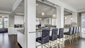 Une cuisine spacieuse avec des meubles blancs, un îlot central et des luminaires suspendus.