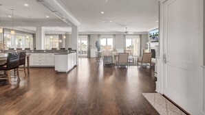 Un vaste espace de vie doté d’un grand plancher en bois, un coin repas avec une table et des chaises, et une cuisine avec des meubles blancs et un îlot central.