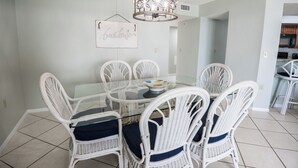 Comedor con una mesa de vidrio rodeada de sillas de mimbre blanco con cojines azules.