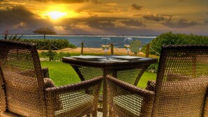 A wicker table and chairs with a view of the ocean and a sunset.