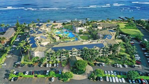 An aerial view of a resort with a large pool, solar panels, and a view of the ocean.