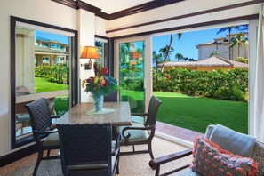 A room with a glass door leading to a well-maintained lawn and a pool, furnished with a table and chairs, and a vase with flowers. - Waipouli Beach Resort Exquisite Grd Fr Pool View (Kapaa)