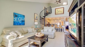 A spacious living room with a modern staircase, a dining area, and a kitchen in the background.