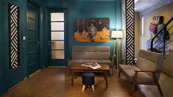 Una habitación con paredes color turquesa, un sofá, una mesa de centro con una revista, una lámpara y una escalera con papel tapiz estampado.