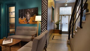 Eine Hotelhalle mit einer Couch, einem kleinen Tisch, einer Lampe, einem Gemälde und einer Treppe.