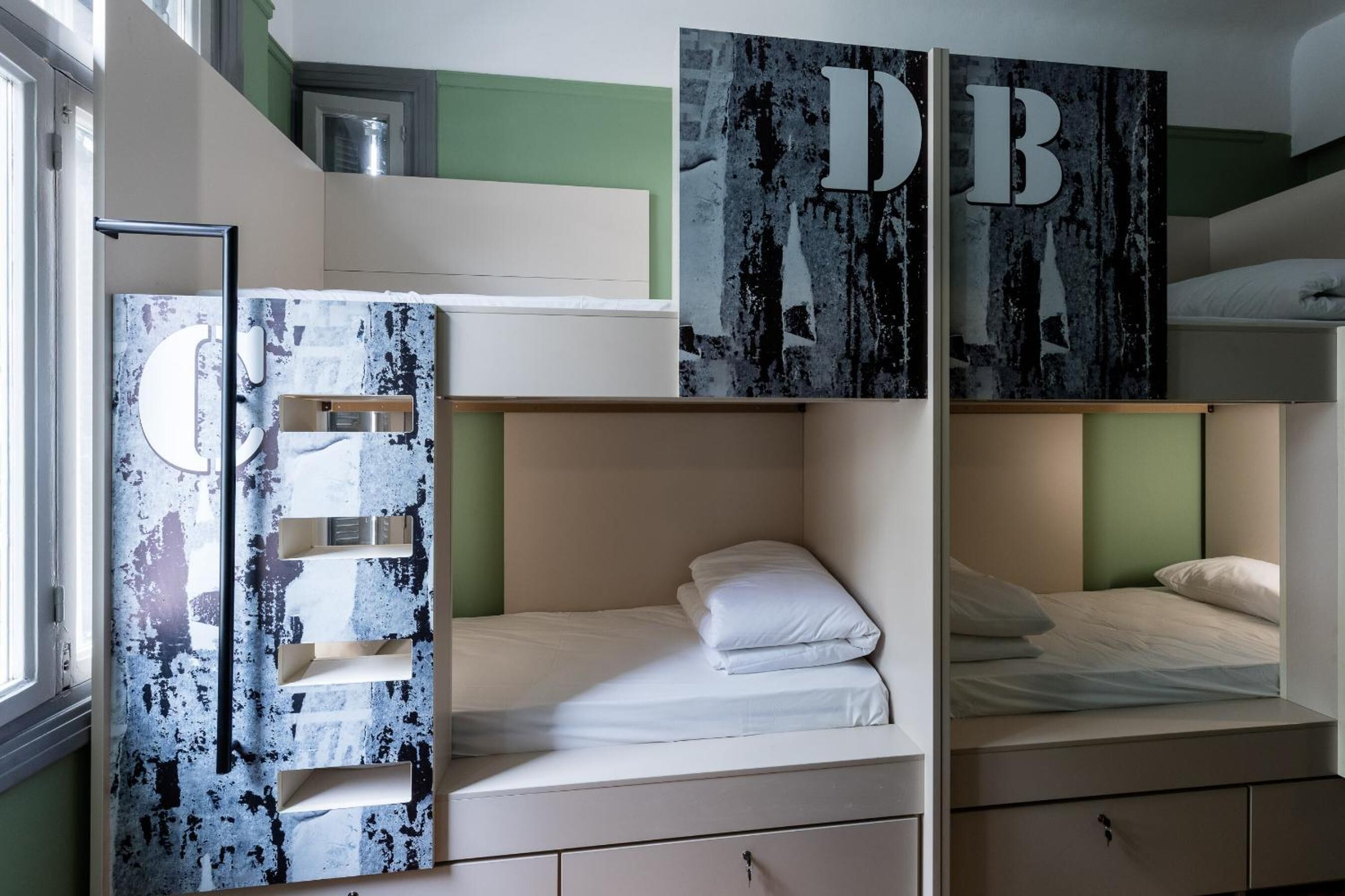 Una habitación con literas, un armario con diseño envejecido y un gran letrero con las iniciales 'DB' en la pared.