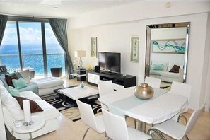 Enjoy a panoramic sea view from the comfort of this stylish room, featuring a seating area, dining table, flat-screen TV, and large mirror.