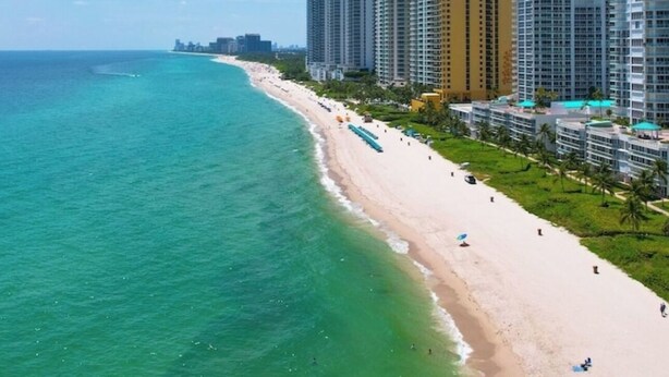A coastal cityscape with high-rise buildings, a sandy beach, and a clear blue sky. - La Perla 5 star Condo  STR-00547 (Sunny Isles Beach)