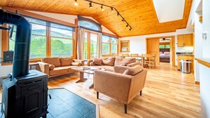A spacious living area with a large sofa, wooden flooring, and a black wood stove.
