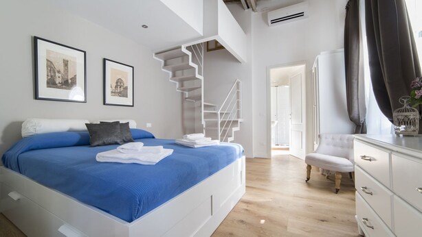 A modern bedroom with a large bed, a white dresser, a chair, a staircase, and two framed pictures on the wall. - Delightful apartment with mezzanine for 4 people, ideal for those who want to visit the city center (Firenze)