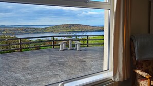 Ein Zimmer mit Blick auf einen See und Hügel. Vier Steintische und ein Stuhl befinden sich vor dem Fenster.