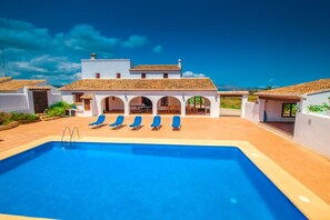 A swimming pool with blue water, surrounded by white buildings with tiled roofs and arches.