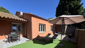 Un patio con césped artificial, una mesa y sillas, dos tumbonas y una parrilla para barbacoa.