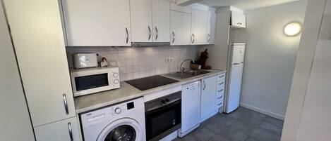 A compact kitchen with white cabinets, a microwave, a toaster, a sink, a dishwasher, and a washing machine.