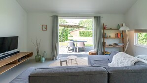 A modern living room with a sofa, TV, and a dining area with chairs and an umbrella.
