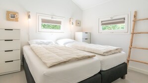 A bedroom with a bed, two bedside tables, a wardrobe, and two windows with blinds.