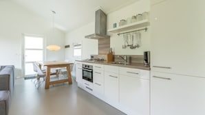 A modern kitchen with white cabinetry, stainless steel appliances, and a dining area with a wooden table and chairs.
