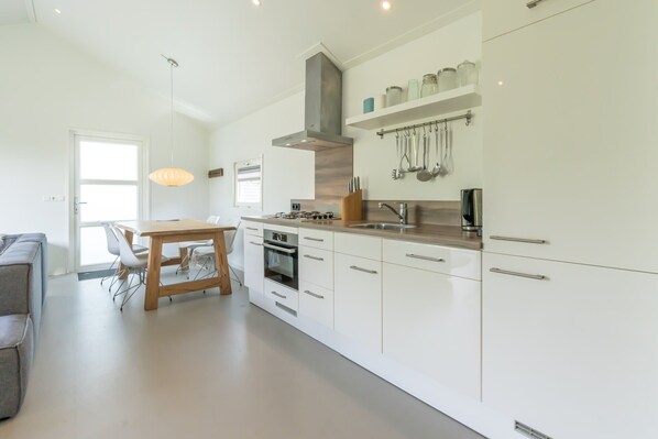 A modern kitchen with white cabinetry, stainless steel appliances, and a dining area with a wooden table and chairs. - Light, pretty skies and lots of space! (BURGH-HAAMSTEDE)