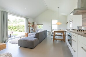 A modern kitchen with a dining area, a sofa, and a view of greenery outside. - Light, pretty skies and lots of space! (BURGH-HAAMSTEDE)