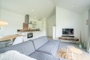 A modern living room with a grey sofa, a dining table, a TV, and a kitchen area in the background. - Light, pretty skies and lots of space! (BURGH-HAAMSTEDE)