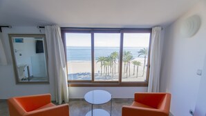 A room with two orange chairs, a small white table, and a large window with a view of the beach and palm trees. - SUPER TORRE - 4 NIVELES CON VISTAS AL MAR (Villajoyosa)
