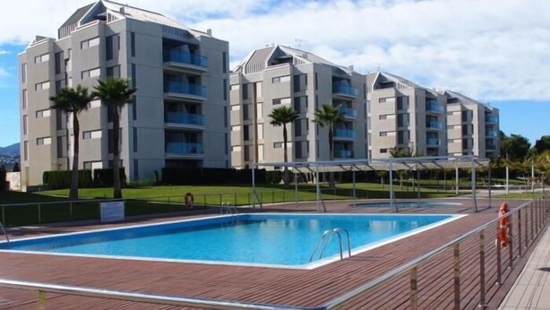 Un moderno edificio de apartamentos con piscina rectangular rodeada por una terraza de madera.