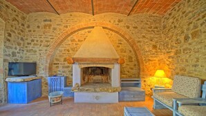 A stone-walled room with a fireplace, a television, and seating. - Borgo - Apartment with pool (Poggibonsi)