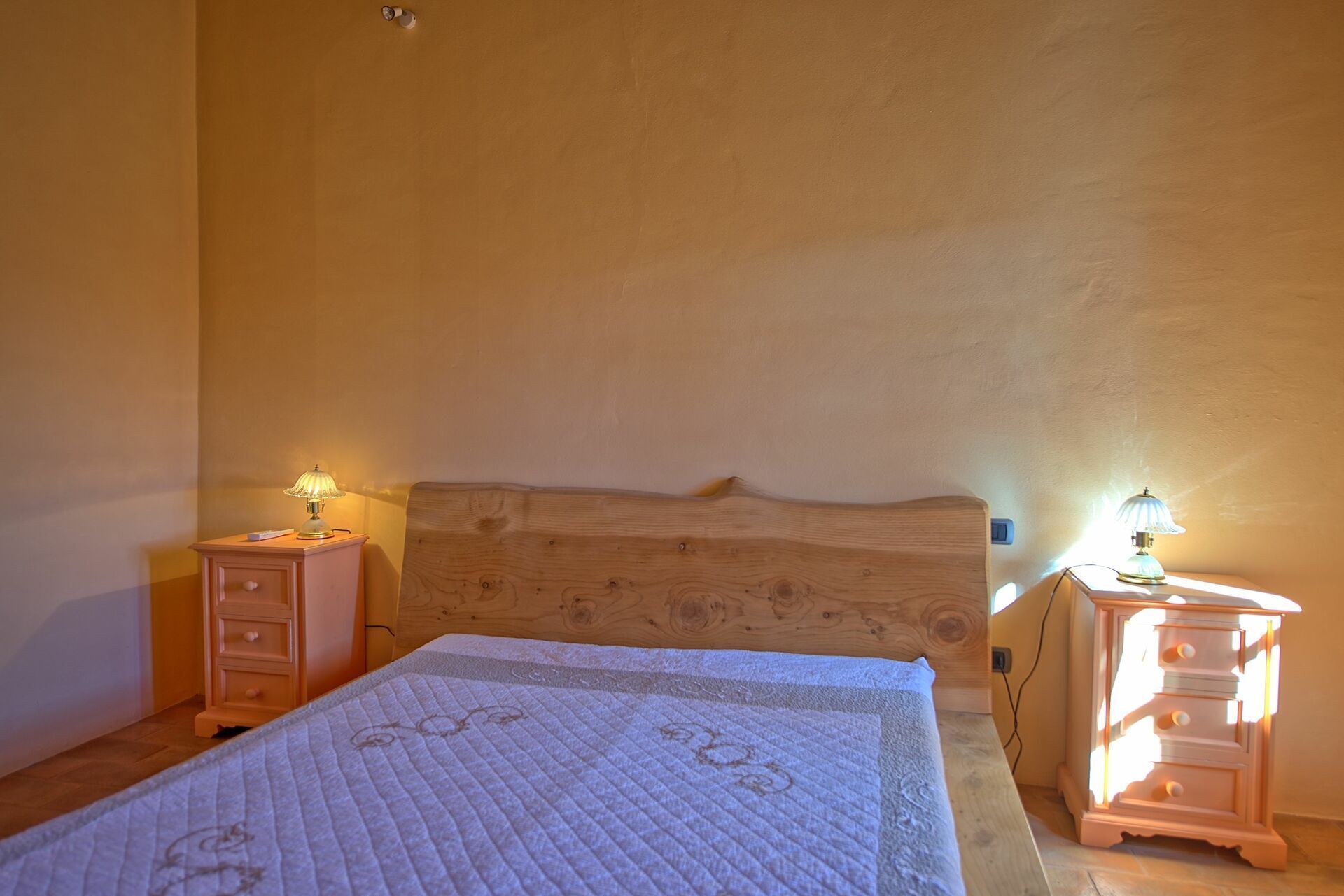 Une chambre à coucher avec une tête de lit en bois, une couvre-lit matelassée et deux tables de chevet avec des lampes.