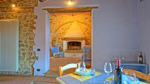 A rustic dining area with a stone fireplace, wooden beams, and a table set for two with wine glasses and a bottle. - Borgo - Apartment with pool (Poggibonsi)