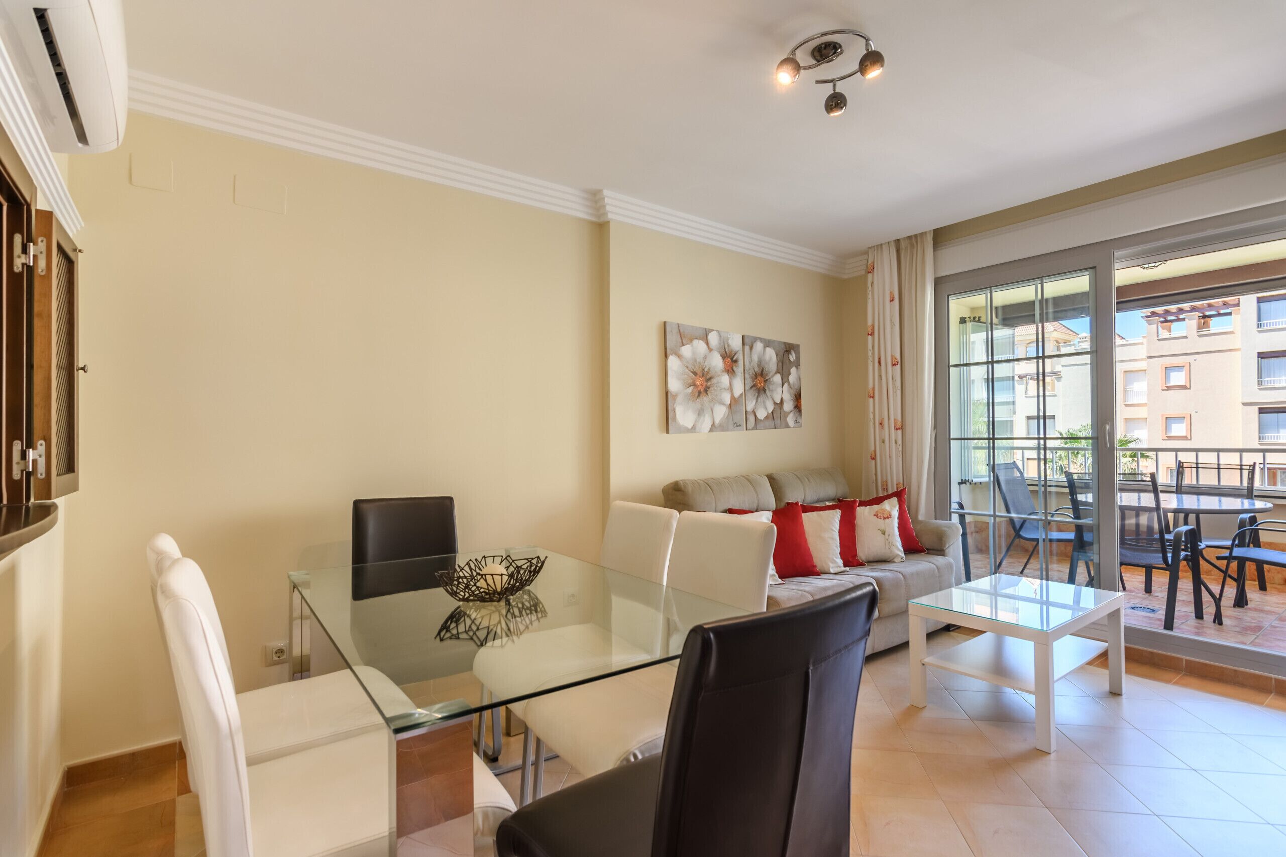 Uma sala de estar moderna com uma mesa de centro de vidro, sofá branco e um espaço de jantar com cadeiras.