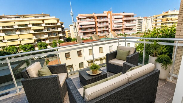 A balcony with wicker furniture, potted plants, and a view of surrounding buildings.