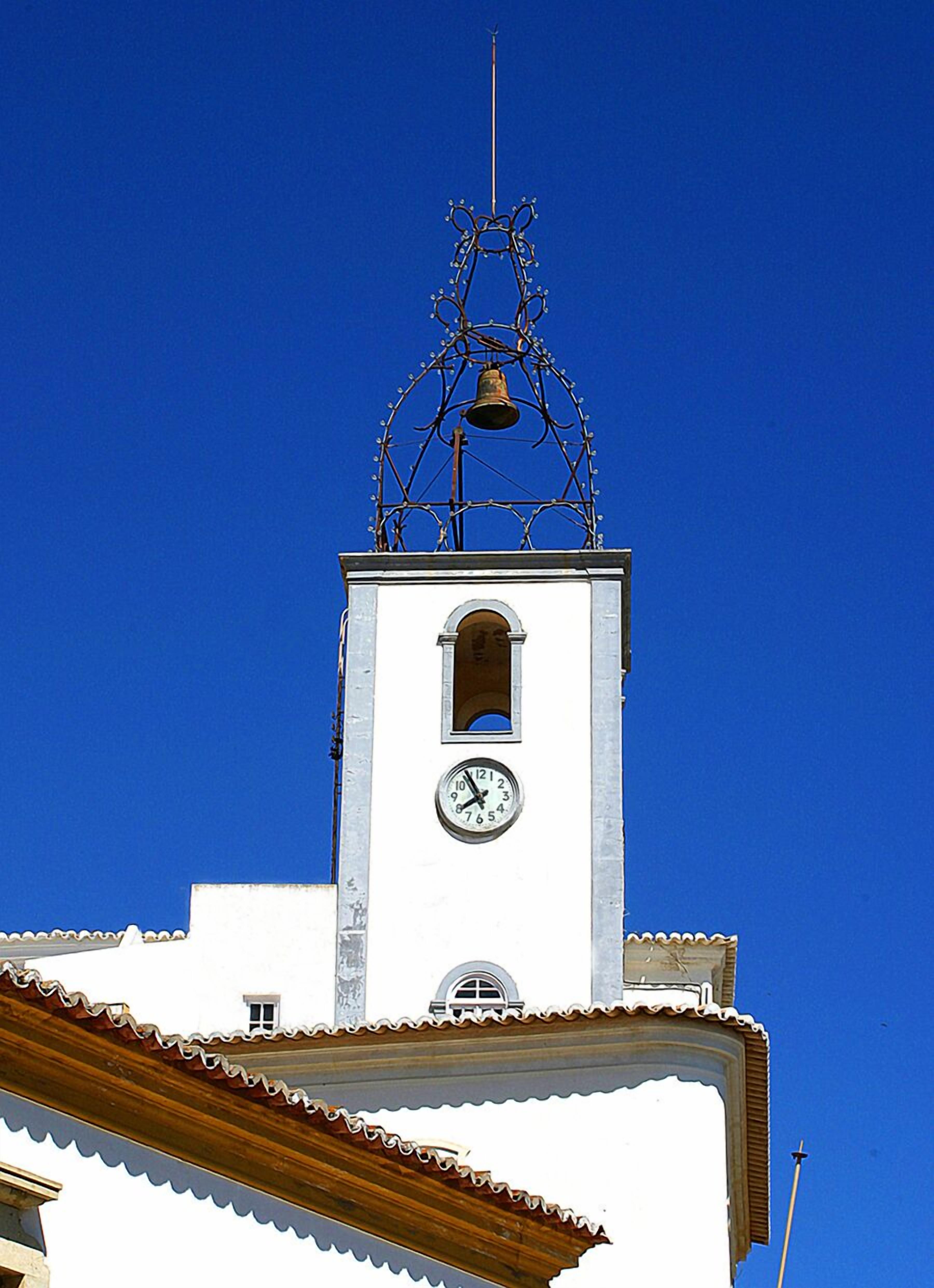 A white church tower with a clock and a bell.