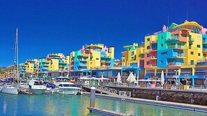 Un port de plaisance avec des bâtiments aux couleurs vives, des bateaux et un ciel bleu azur.
