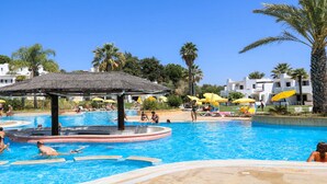 Un espace piscine agrémenté d’un gazebo à toit de chaume, de chaises longues et de parasols.