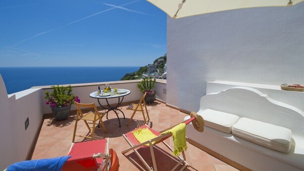 Une terrasse avec une table et des chaises, un canapé blanc et une vue sur la mer.