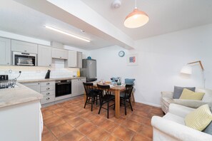 A modern kitchen with white cabinets, a dining table with chairs, and a sofa in a living area.