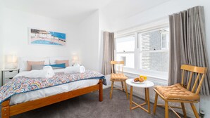 Ett hotellrum med en säng, en stol, ett litet bord och ett fönster med gardiner.